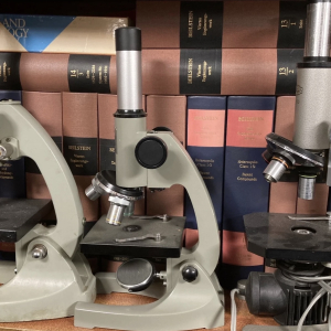 Vintage brass and black microscope with old books – period lab prop